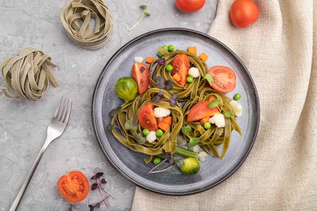 Tagliatelle green spinach pasta with tomato, pea and microgreen sprouts on a gray concrete surface and linen textile