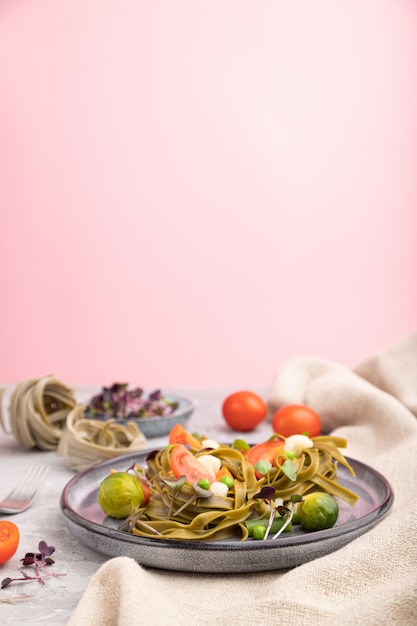 Tagliatelle green spinach pasta with tomato, pea and microgreen sprouts on a gray and pink background. Side view,selective focus, copy space.