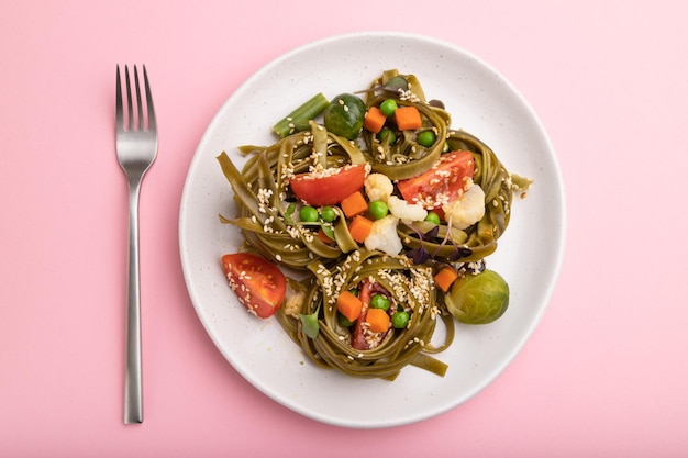 Tagliatelle groene spinaziepasta met tomatenerwt en microgroene spruiten op een pastelroze achtergrond Bovenaanzicht close-up