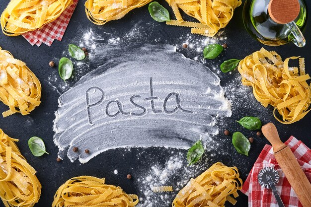 Tagliatelle. Homemade pasta, basil leaves, flour, pepper, olive oil and cherry tomato on dark black background. Food concept. Mock up. Horizontal with copy space.