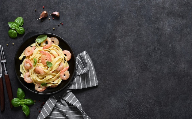 Tagliatelle pasta met romige saus en garnalen in een koekenpan op de keukentafel op een zwarte achtergrond. uitzicht van boven.