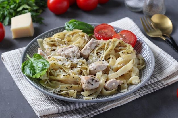 Tagliatelle pasta with chicken and cheese served with cherry tomatoes and basil on gray background