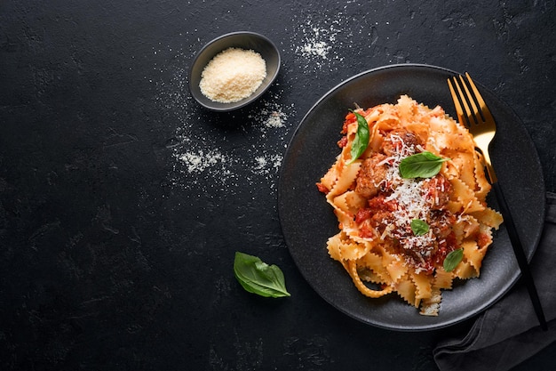 Tagliatelle pasta with meatballs in tomato sauce, basil and parmesan cheese on black stone or concrete background. Traditional Italian dish and cuisine. Top view with copy space.