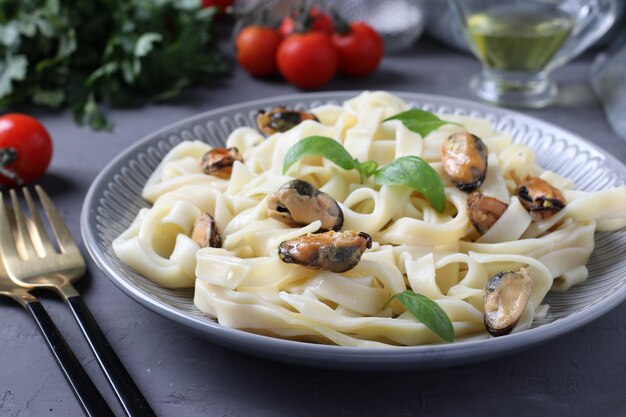 Tagliatelle pasta with mussels and basil on a plate on gray background.