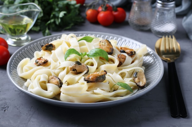 Tagliatelle pasta with mussels and basil on a plate on gray surface. Close up