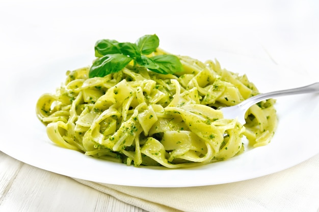 Tagliatelle al pesto, basilico e forchetta in un piatto su un asciugamano sullo sfondo di assi di legno