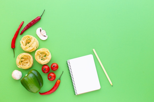 Тальятелле сырые макаронные изделия и овощи на зеленом фоне, вид сверху Копировать рецепт приготовления пространства
