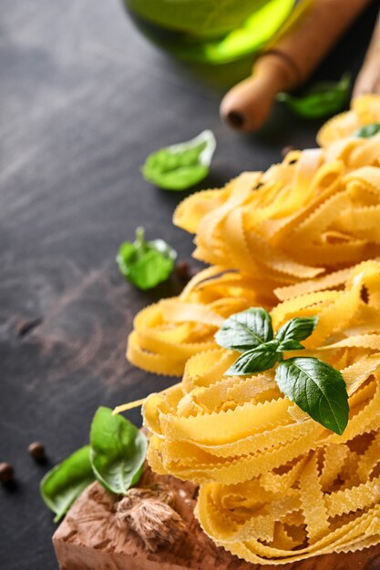 Tagliatelle. Zelfgemaakte pasta, basilicumblaadjes, bloem, peper, olijfolie, cherrytomaat en deegroller en pastames op donkere oude houten achtergrond. Voedselconcept. Bespotten. Horizontaal met kopie ruimte.