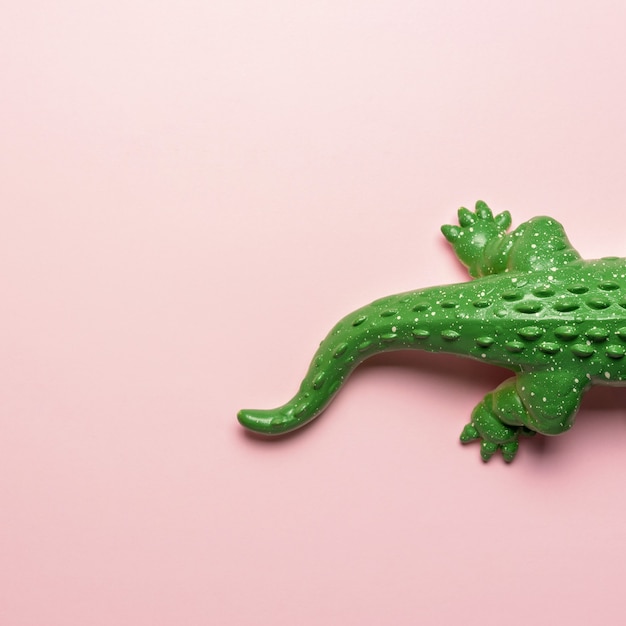 Tail of green crocodile toy on pastel pink background.