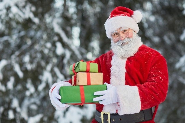 Taille omhoog portret van de traditionele kerstman die cadeautjes buiten in het winterbos vasthoudt en glimlacht