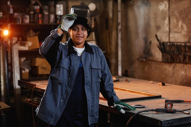 Taille omhoog portret van multi-etnische vrouwelijke lasser die lacht naar de camera in de industriële fabrieksworkshop