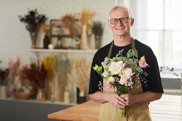 Taille omhoog portret van senior man die bloemen vasthoudt in de bloemenwinkel en naar de kopieerruimte van de camera kijkt