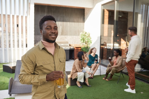 Taille portret van jonge afro-amerikaanse man en glimlachen terwijl staande op terras tijdens buitenfeest,