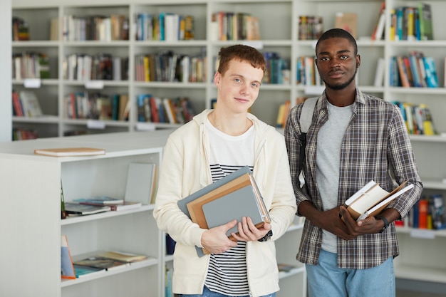 Taille portret van twee jonge mannen in de schoolbibliotheek boeken te houden en gelukkig glimlachen naar de camera,