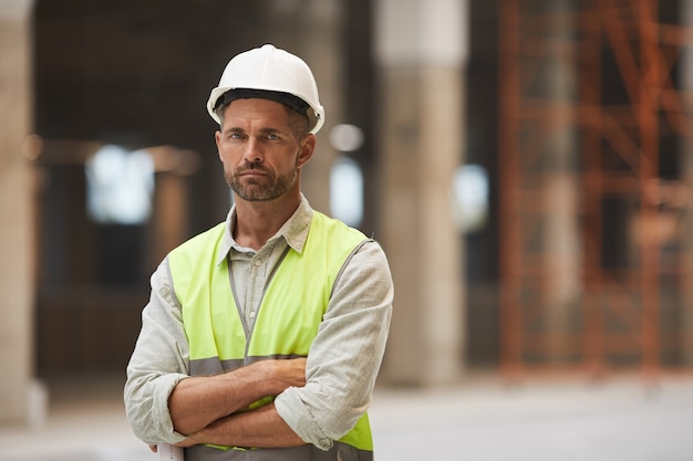 Taille portret van volwassen bouwvakker terwijl staande met gekruiste armen op de bouwplaats,