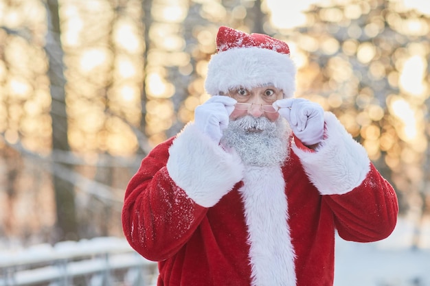 Taille-up portret van de traditionele kerstman die naar de camera kijkt over een bril en er verrast uitziet