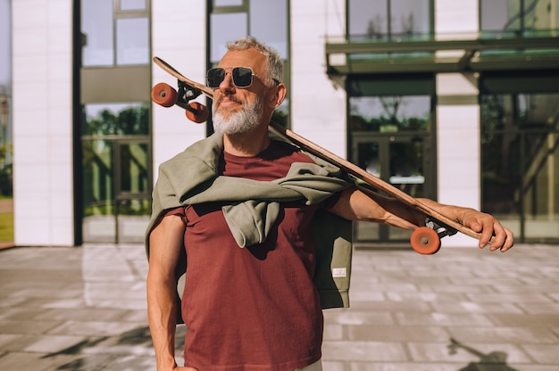 Taille-up portret van een grijsharige bebaarde atletische man met het skateboard starend in de verte