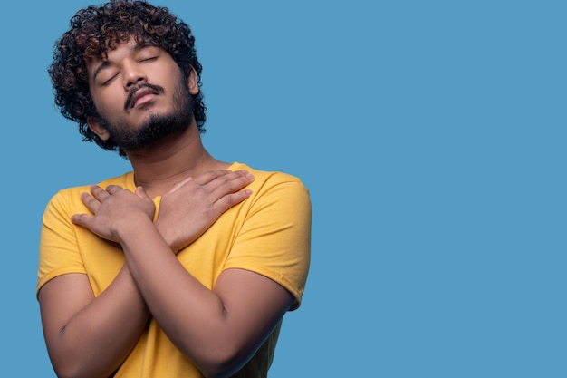 Taille-up portret van een hindoe-man met zijn ogen dicht poseren tegen de blauwe achtergrond