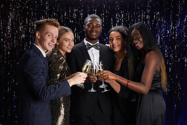 Taille-up portret van een multi-etnische groep vrienden rammelende champagneglazen en lachend naar de camera terwijl u geniet van een elegant feest