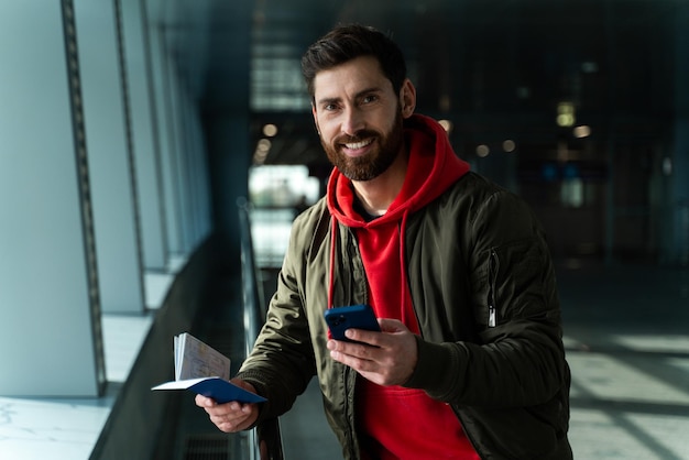 Taille-up portret van geconcentreerde jonge man die op de luchthaven staat en zijn smartphone vasthoudt terwijl hij op vertrek wacht. technologieën en mensen concept