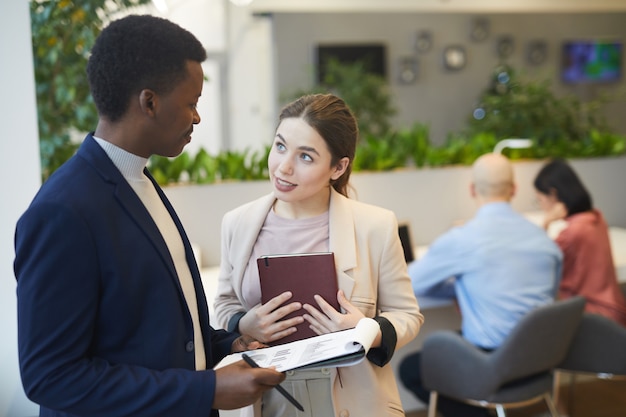 Taille-up portret van jonge enthousiaste zakenvrouw in gesprek met manager tijdens het bespreken van werkproject