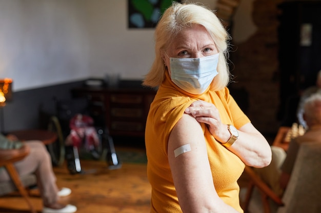 Taille-up portret van senior vrouw met masker die schouder naar camera toont na vaccinatie tegen COVID 19