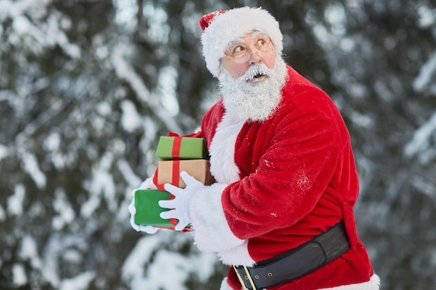 Taille-up portret van traditionele kerstman die cadeautjes in het geheim buiten draagt en er voorzichtig uitziet