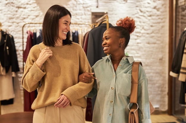 Taille-up portret van twee jonge vrouwen die samen winkelen en naar de camera lopen en naar elkaar glimlachen