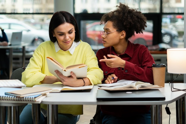 Taille-up portretweergave van de gelukkige jonge universiteitsstudenten die studeren met boeken in de bibliotheek Groep multiraciale mensen in de universiteitsbibliotheek