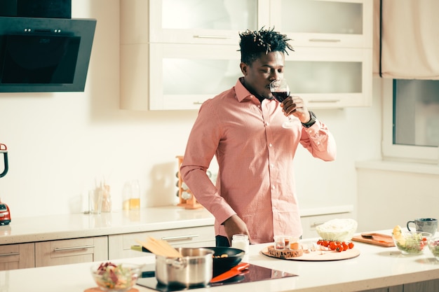 Taille van jonge man die in de keuken staat met een glas rode wijn