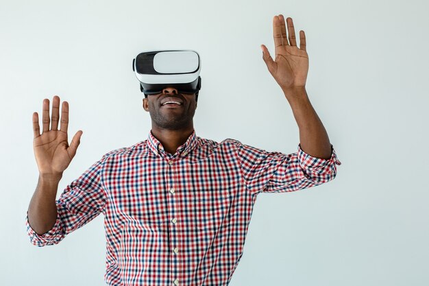 Taille van vrolijke glimlachende afro-Amerikaanse man die VR-gadget test terwijl hij tegen een witte muur staat