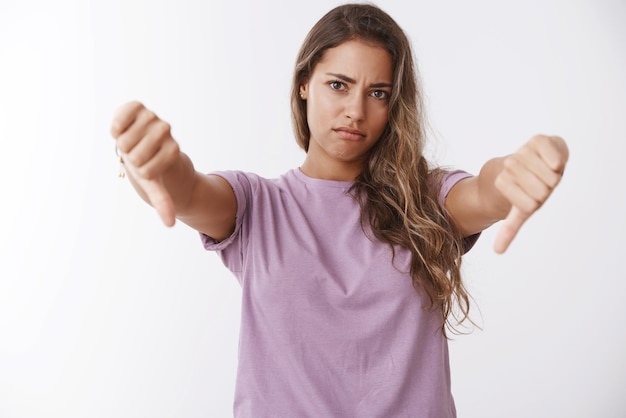 Foto taille veroordelend ontevreden jonge vrouw grimassen teleurgesteld tonen duimen naar beneden oneens totaal afkeuren boos zijn slechte verwende prestaties fronsen somber staand witte achtergrond