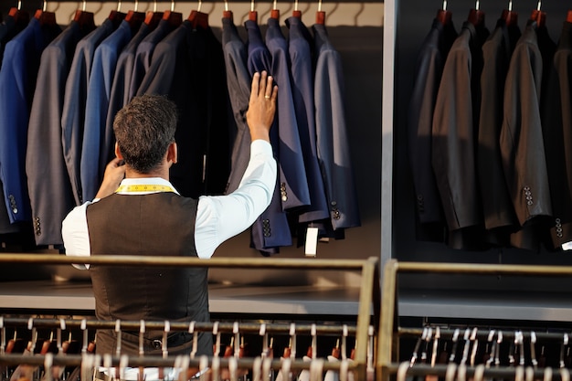 Tailor checking finished bespoke jackets hanging on rail in his atelier