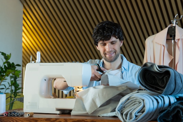 Tailor cutting fabric man working with sewing machine in a textile studio