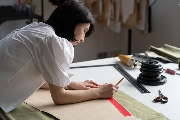 仕立て屋または洋裁の女性は、職場で若い女性デザイナーをカットして縫うために生地にパターンをスケッチします