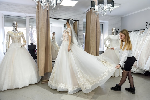 Tailor in wedding salon helping bride to try on  dress