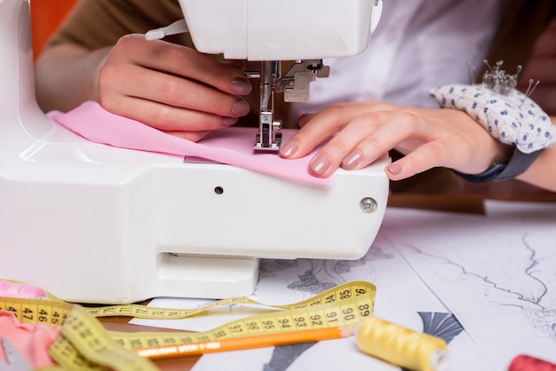 Tailor working on sewing machine. Close-up of female fashion designer working on sewing machine while sitting at her working place