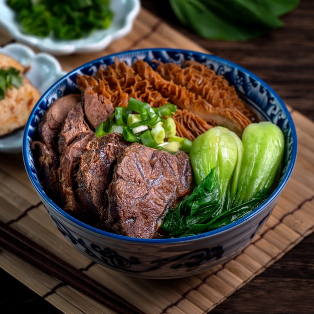 사진 나무 테이블 배경에 얇게 썬 찐 쇠고기 정강이, 내장 및 야채와 함께 대만의 유명한 음식 쇠고기 국수.