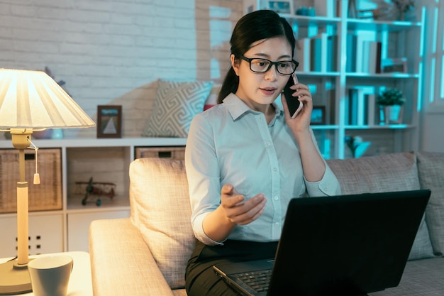 taiwanese female employee is using laptop and explaining content of financial statement to her boss on phone . professional looking asian lady is working overtime at home.