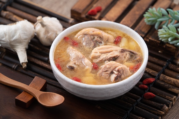 Тайваньская еда - домашний вкусный чесночный куриный суп в миске на фоне темного деревянного стола.