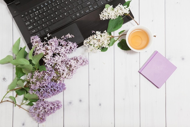 Tak van lila bloemen met pad-laptop en kopje thee op een wit bureaublad plat uitzicht