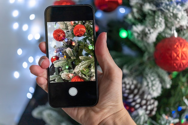 クリスマスツリーの鮮やかな美しい写真を撮ります。ブロガーはソーシャルメディアを狙っています。雪の中で美しいクリスマスツリー。
