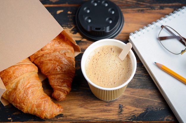 Take away coffee cup with croissant on wooden table.