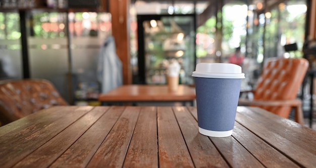 Take Away coffee cup on wooden table with blurred cafe background.