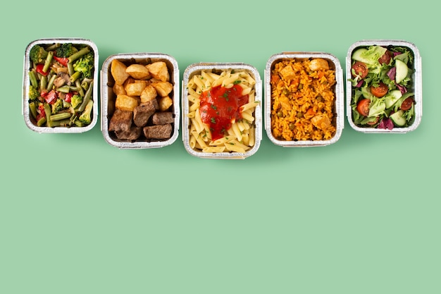 Take away healthy food in foil boxes on green background