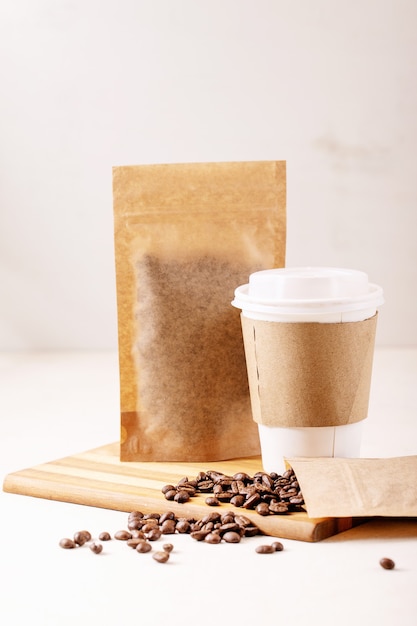 Take away paper cup, coffee beans and coffee packs with blank space for logo over white wall. Copy space