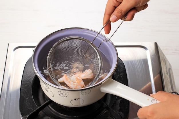 Prendi gamberi o gamberi freschi bolliti con un colino processo di cottura in cucina mano femminile asiatica che prepara una deliziosa ricetta per involtini primavera vietnamiti