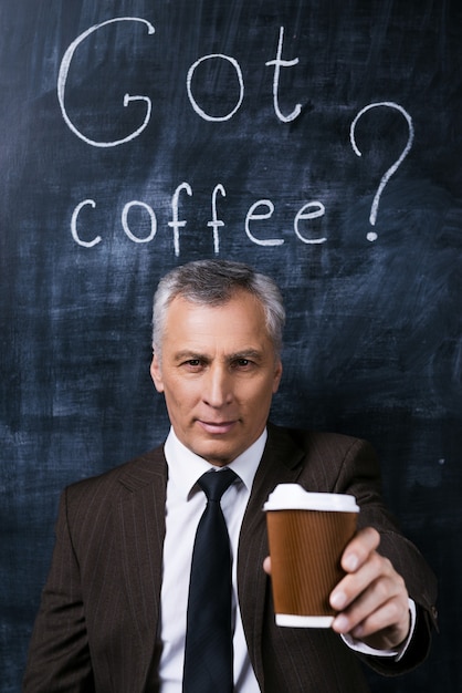 休憩する！コーヒーカップを伸ばして、チョークで描かれた黒板に立って笑っている正装で自信を持って年配の男性