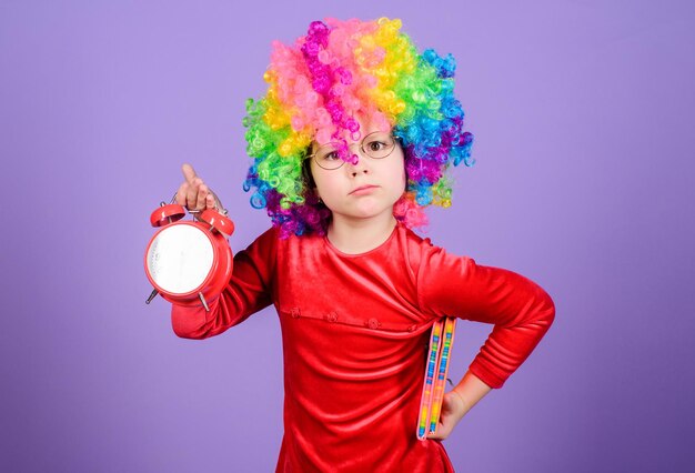 Take care of your time Girl cute playful kid wear curly rainbow wig Life is fun Happy childhood Happy little girl International childrens day Child care Happy moments Kid hold alarm clock