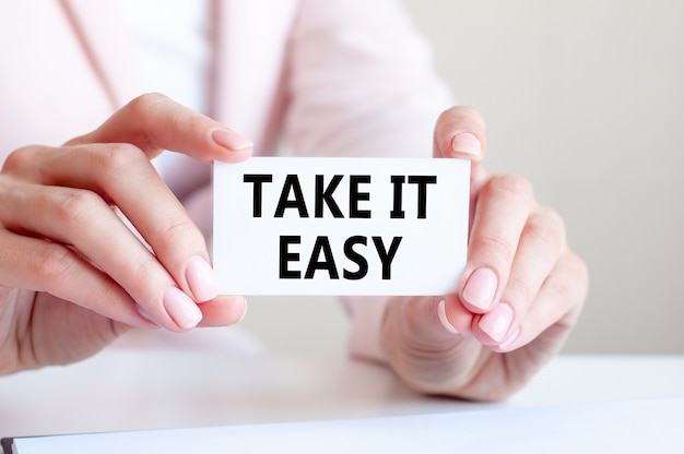 TAKE IT EASY is written on a white business card in a woman's hands